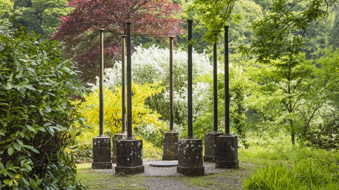 Cofeb Pamela Chance yng Ngardd Goedwig Colby, Sir Benfro, sy’n cynnwys saith piler mewn cylch yn sefyll ymysg y coed.